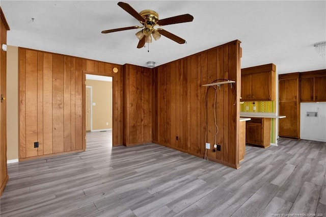 unfurnished living room with ceiling fan, light hardwood / wood-style floors, and wood walls