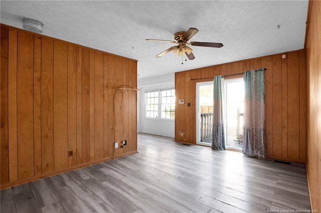 spare room with ceiling fan, wooden walls, a textured ceiling, and light wood-type flooring