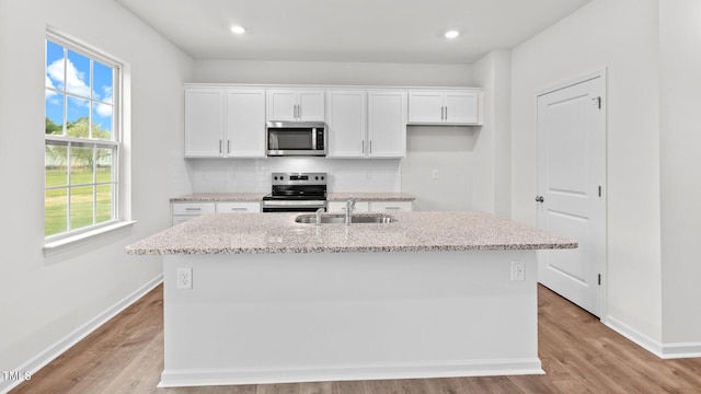 kitchen with sink, tasteful backsplash, appliances with stainless steel finishes, a kitchen island with sink, and white cabinets