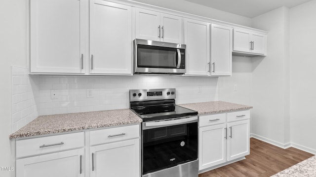 kitchen featuring white cabinetry, light stone counters, light hardwood / wood-style flooring, stainless steel appliances, and backsplash