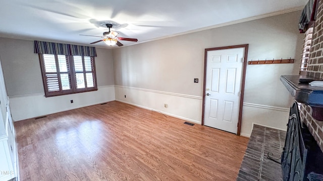 interior space featuring ceiling fan, ornamental molding, a brick fireplace, and light wood-type flooring