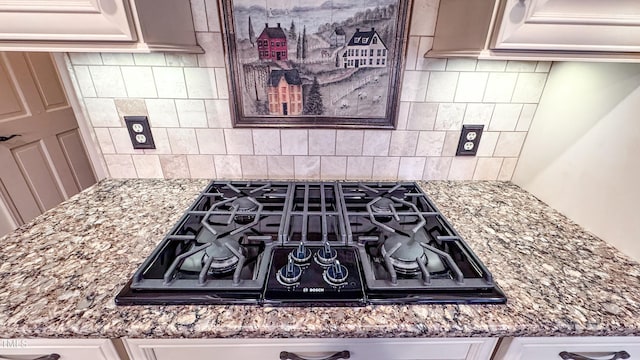 interior details featuring light stone counters, decorative backsplash, and black gas cooktop