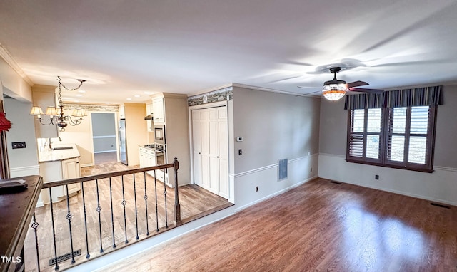 unfurnished room with crown molding, sink, ceiling fan with notable chandelier, and hardwood / wood-style floors