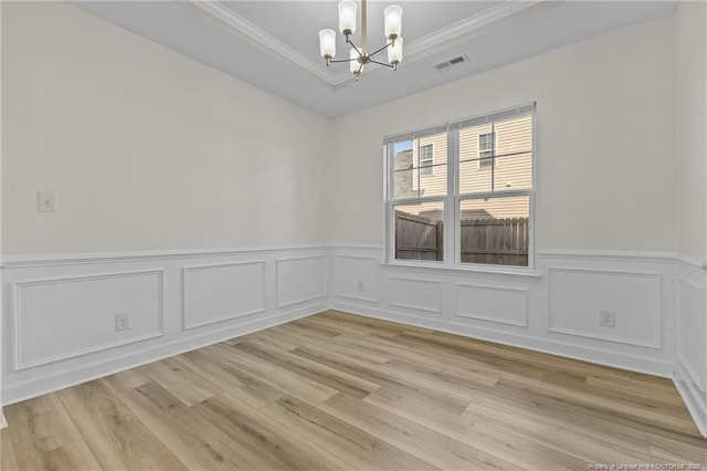 empty room featuring ornamental molding, a raised ceiling, a chandelier, and light wood-type flooring