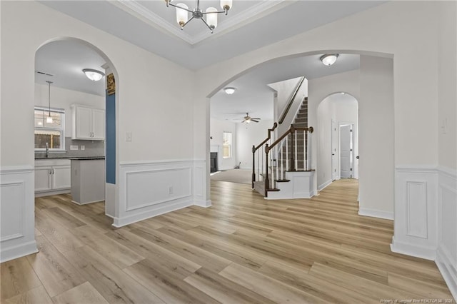 entryway featuring sink, crown molding, light hardwood / wood-style floors, ceiling fan with notable chandelier, and a raised ceiling