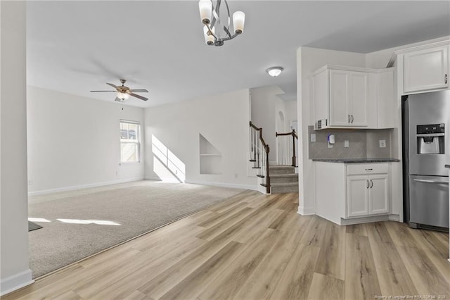 kitchen with stainless steel refrigerator with ice dispenser, white cabinetry, tasteful backsplash, light hardwood / wood-style flooring, and ceiling fan with notable chandelier