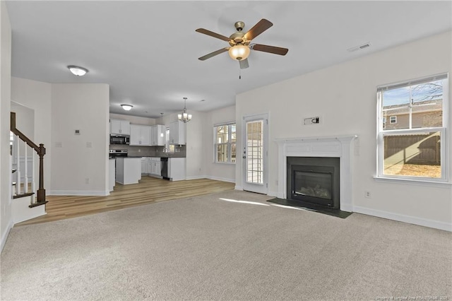 unfurnished living room with light colored carpet and ceiling fan with notable chandelier