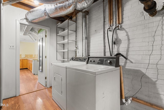 clothes washing area with brick wall, light wood-type flooring, and independent washer and dryer