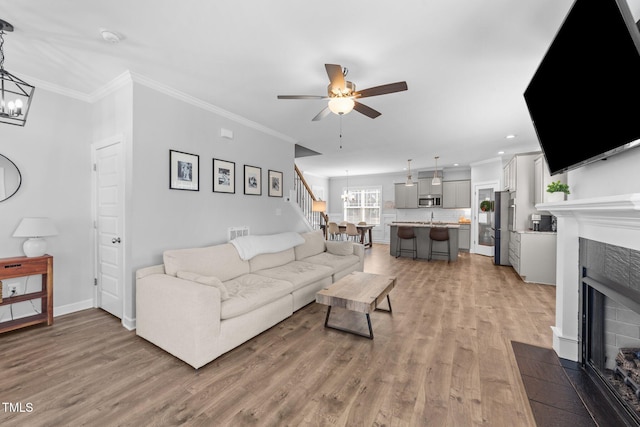 living room with hardwood / wood-style flooring, a fireplace, ornamental molding, and ceiling fan with notable chandelier