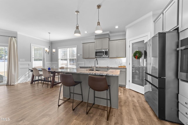 kitchen featuring gray cabinetry, stainless steel appliances, light stone counters, an island with sink, and decorative light fixtures