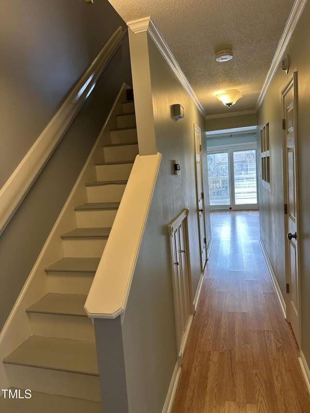 staircase with crown molding, wood-type flooring, and a textured ceiling