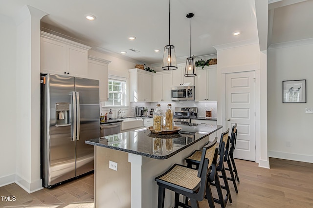 kitchen featuring crown molding, appliances with stainless steel finishes, white cabinetry, a kitchen island, and dark stone counters