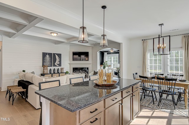 kitchen with coffered ceiling, hanging light fixtures, light wood-type flooring, a kitchen island, and dark stone counters