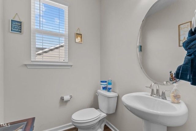 half bathroom featuring toilet, baseboards, and a sink