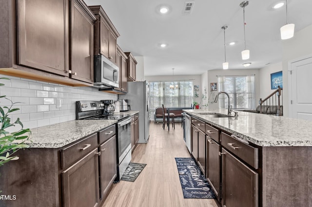 kitchen featuring dark brown cabinetry, stainless steel appliances, a sink, light wood-type flooring, and backsplash