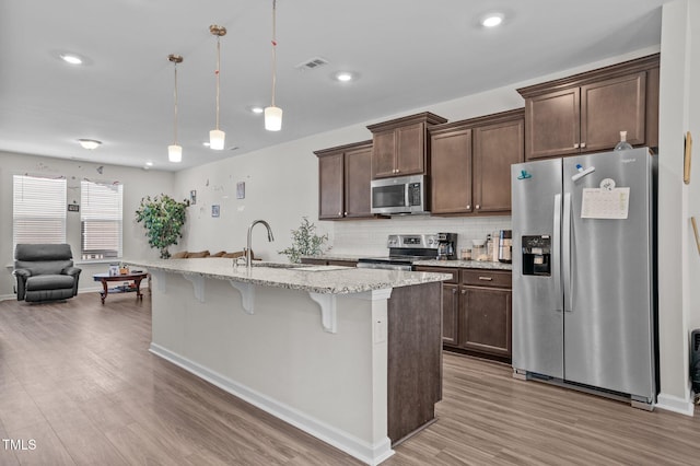 kitchen with a breakfast bar area, wood finished floors, a sink, appliances with stainless steel finishes, and tasteful backsplash