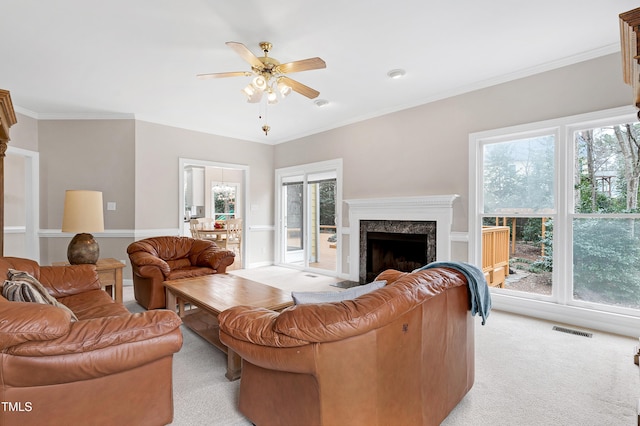 carpeted living room featuring a high end fireplace, ornamental molding, and ceiling fan