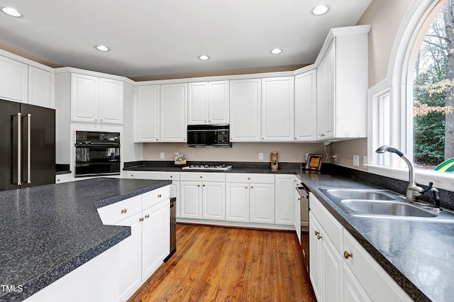 kitchen with hardwood / wood-style flooring, sink, white cabinets, and black appliances