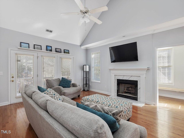 living room featuring ceiling fan, a high end fireplace, high vaulted ceiling, and light hardwood / wood-style flooring