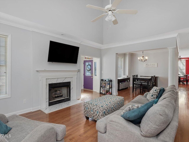 living room featuring crown molding, a high end fireplace, wood-type flooring, and ceiling fan with notable chandelier