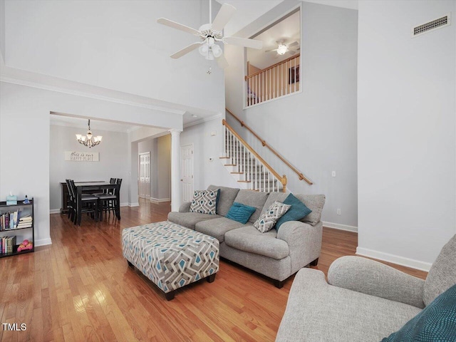 living room with hardwood / wood-style flooring, ornamental molding, ceiling fan with notable chandelier, and a high ceiling