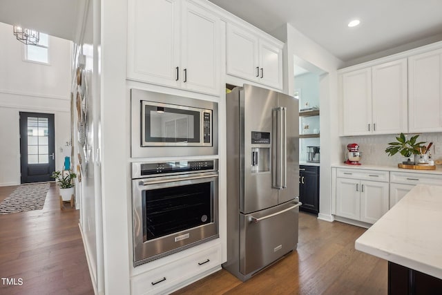 kitchen featuring stainless steel appliances, white cabinetry, dark wood-type flooring, and decorative backsplash