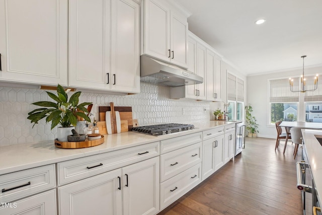 kitchen featuring dark wood-type flooring, pendant lighting, stainless steel gas stovetop, decorative backsplash, and white cabinets