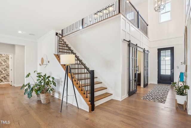 entrance foyer featuring wood-type flooring, a chandelier, a high ceiling, crown molding, and a barn door