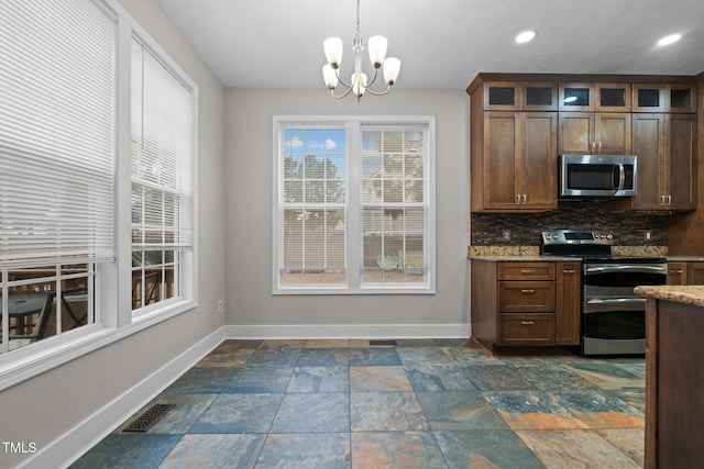 kitchen featuring light stone counters, an inviting chandelier, hanging light fixtures, appliances with stainless steel finishes, and backsplash