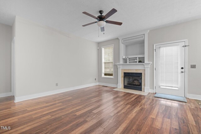 unfurnished living room featuring a tiled fireplace, hardwood / wood-style floors, a textured ceiling, and ceiling fan