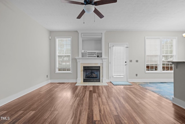 unfurnished living room with ceiling fan, a fireplace, a textured ceiling, and light wood-type flooring