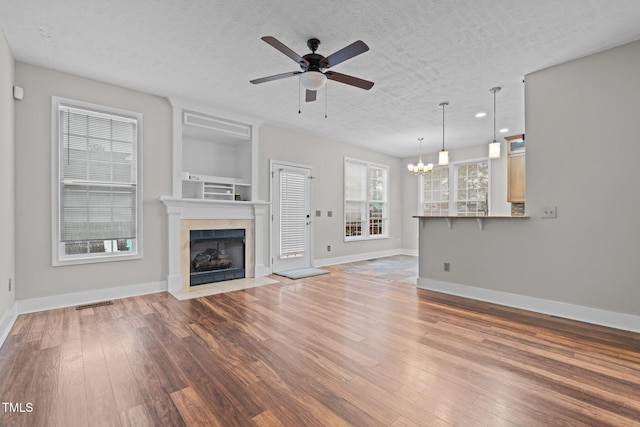 unfurnished living room with a fireplace, ceiling fan with notable chandelier, light hardwood / wood-style flooring, and a textured ceiling