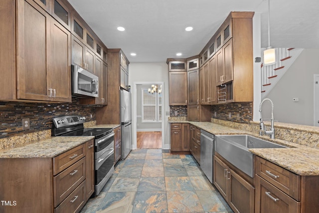 kitchen with stainless steel appliances, hanging light fixtures, sink, and light stone counters