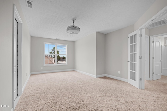 spare room with light colored carpet, a textured ceiling, and french doors