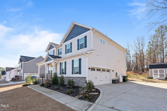 view of side of property with a storage unit, a porch, concrete driveway, an attached garage, and stone siding