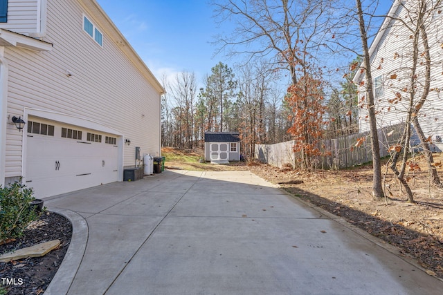 view of side of property with a garage, concrete driveway, an outbuilding, fence, and a shed