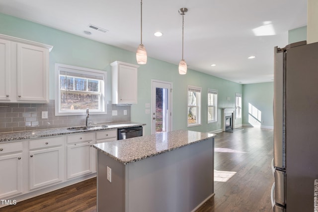 kitchen with light stone counters, stainless steel appliances, a sink, white cabinets, and pendant lighting