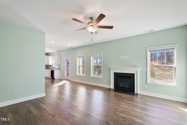 unfurnished living room with dark wood-type flooring, a healthy amount of sunlight, visible vents, and baseboards