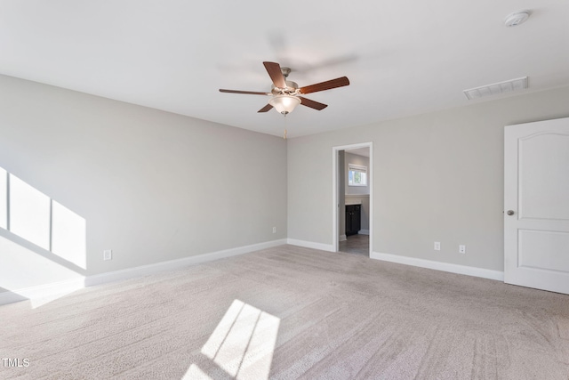 spare room featuring light carpet, ceiling fan, visible vents, and baseboards