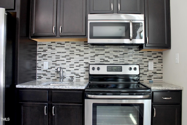 kitchen with light stone counters, decorative backsplash, stainless steel appliances, and a sink