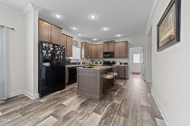 kitchen with wood-type flooring, a kitchen island, a kitchen bar, and black appliances