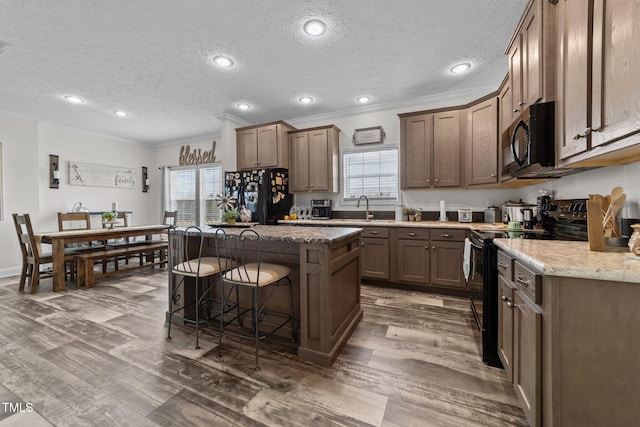 kitchen featuring dark wood-type flooring, sink, light stone counters, a kitchen island, and black appliances