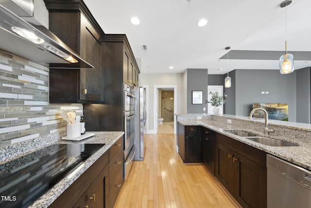 kitchen featuring sink, light stone counters, decorative light fixtures, stainless steel appliances, and wall chimney range hood