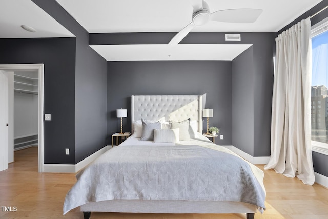 bedroom featuring a walk in closet, ceiling fan, and light hardwood / wood-style flooring