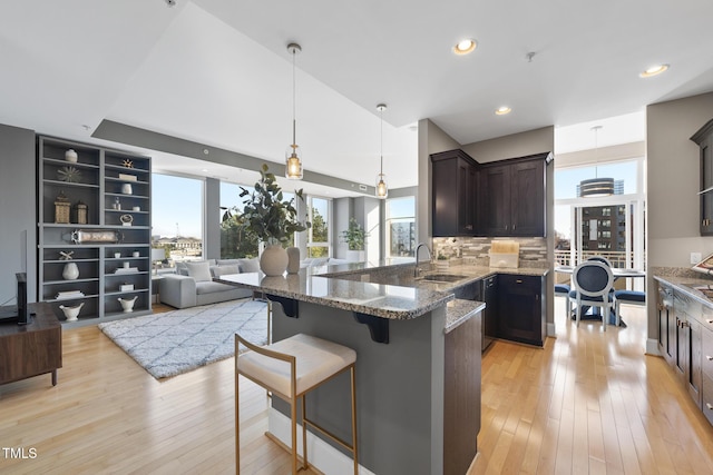 kitchen with pendant lighting, sink, a breakfast bar area, light hardwood / wood-style floors, and dark stone counters