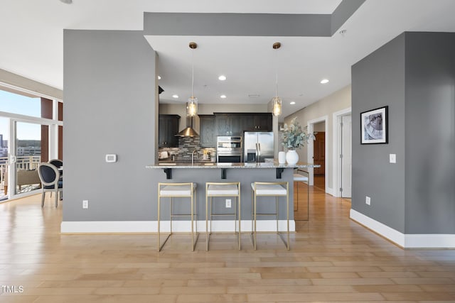 kitchen with a kitchen bar, light stone countertops, hanging light fixtures, and appliances with stainless steel finishes