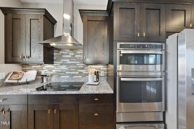 kitchen featuring light stone countertops, decorative backsplash, stainless steel appliances, and wall chimney exhaust hood