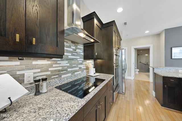 kitchen featuring black electric stovetop, decorative backsplash, light stone countertops, and wall chimney exhaust hood