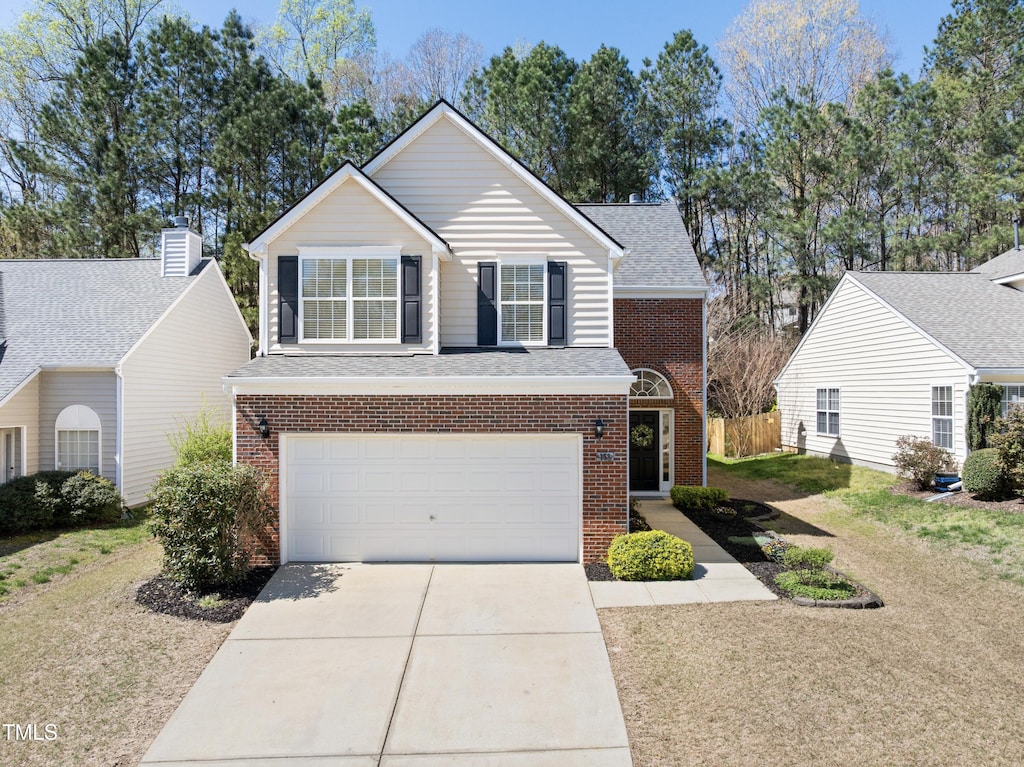 traditional home featuring brick siding, a garage, concrete driveway, and a front yard