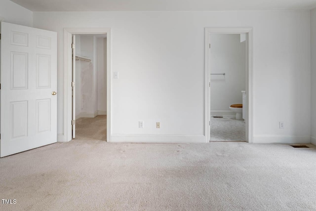 unfurnished bedroom featuring a spacious closet, baseboards, carpet flooring, ensuite bathroom, and a closet